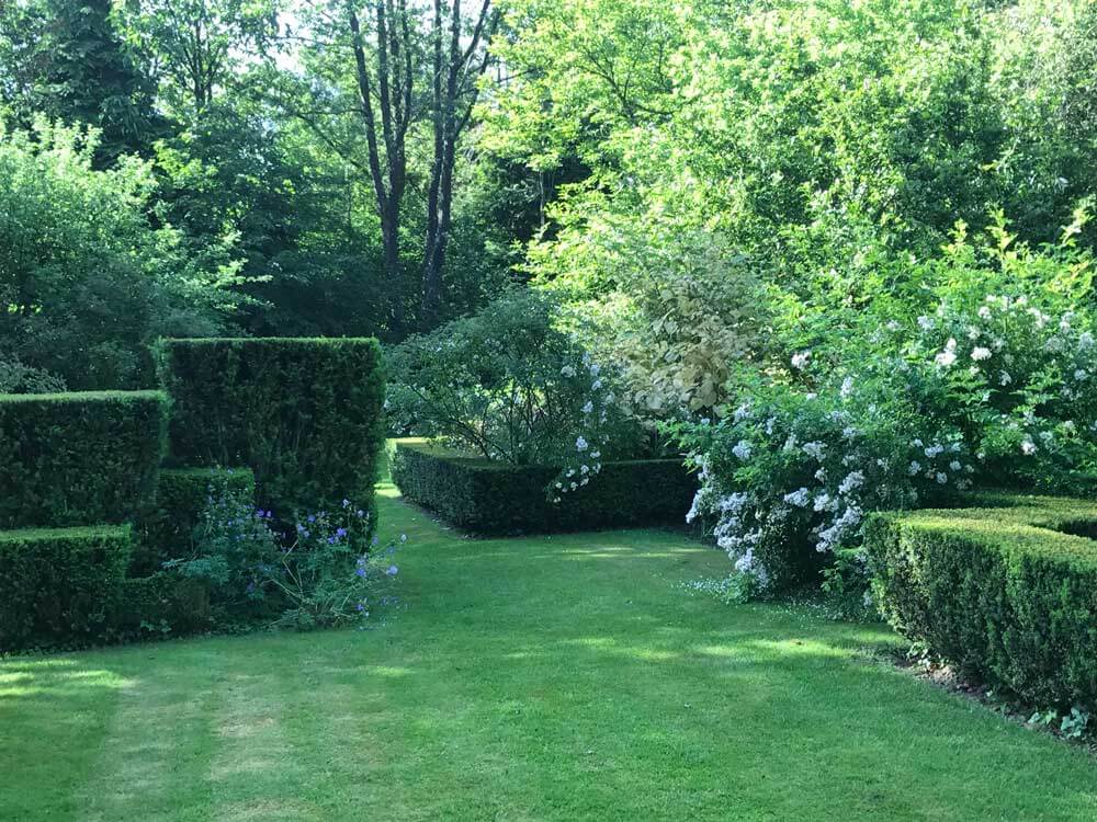 vue d'un jardin français aux nuances de blanc et vert avec des haies d'ifs de hauteurs différentes